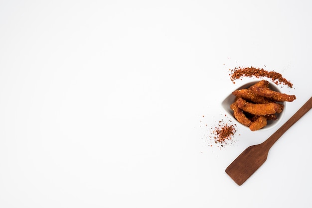 Trozos de carne frita con especias y espátula en mesa gris