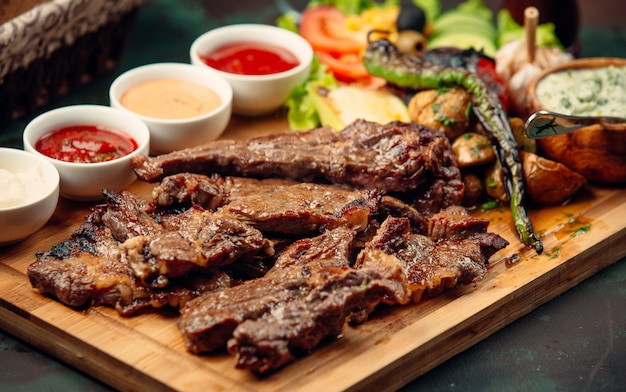 trozos de filete de cordero con salsas, pimiento asado, ensalada fresca sobre tabla de madera