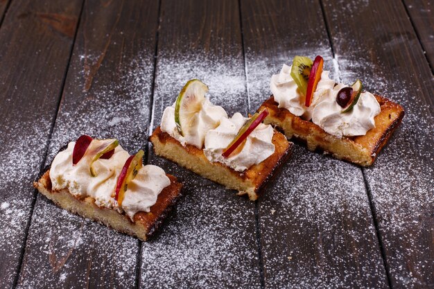 Trozos de pastel con frutas cubiertas con azúcar en polvo servido en una mesa de madera