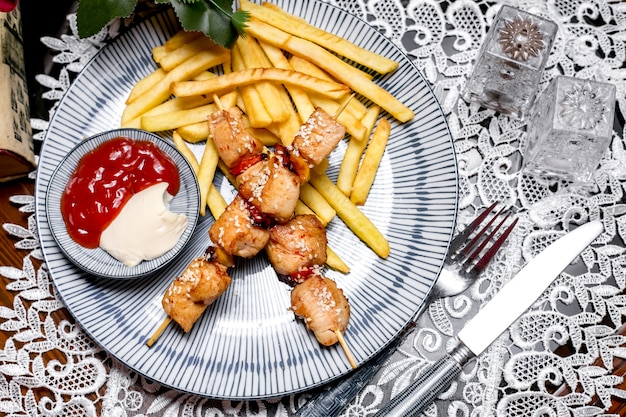 Trozos de pollo en brochetas servidos con papas fritas, mayonesa y salsa de tomate