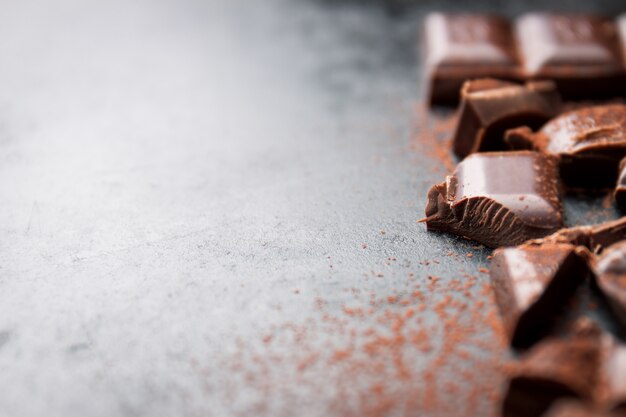 Trozos de tableta de chocolate sobre una mesa de madera negra y cacao espolvoreado encima