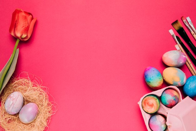 Tulipán rojo Huevo de Pascua nido y pinceles sobre el fondo rosa