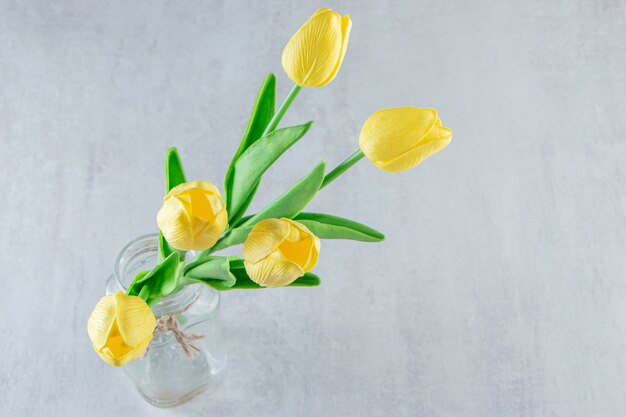 Tulipanes amarillos en un frasco, sobre la mesa blanca.