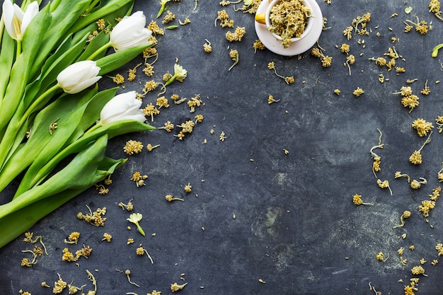 tulipanes blancos con flores secas en una taza sobre una superficie negra