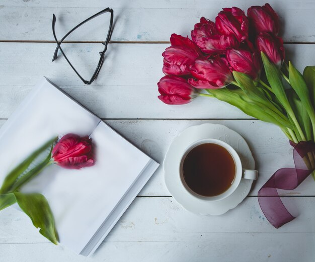 Tulipanes de Borgoña, vasos, una taza de té y un diario.