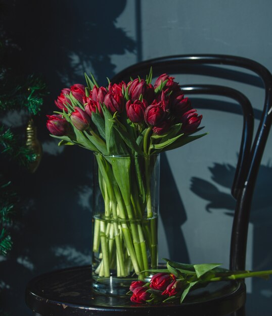 Tulipanes frescos rojos dentro del florero de cristal con agua en una silla.