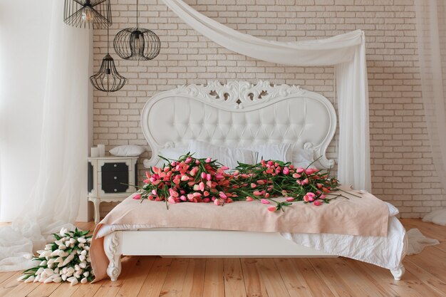 Tulipanes hermosos rojos y blancos en cama clásica grande en fondo de la pared de ladrillo