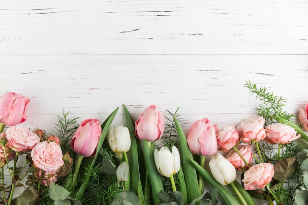 Tulipanes rosados y rosas sobre fondo de tablón de madera