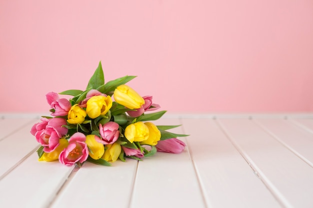 Foto gratuita tulipanes sobre superficie de madera blanca y fondo rosa