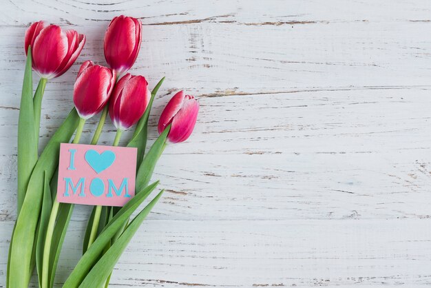 Tulipanes y tarjeta para el día de la madre sobre superficie de madera