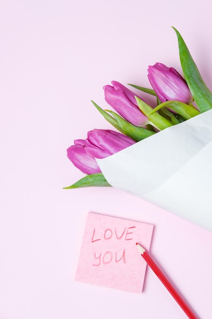 Tulipanes violetas y tarjeta de felicitación sobre un fondo rosa Concepto de primavera Vista superior espacio de copia plana