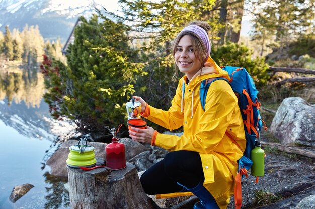 La turista alegre vierte bebida aromática caliente de la cafetera, tiene una aventura de campamento