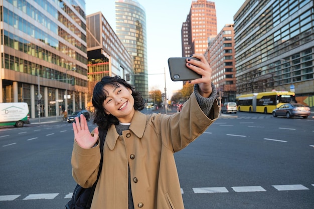 Una turista asiática feliz se toma una selfie en el centro de la ciudad hace una videollamada y saluda a la cámara del teléfono inteligente