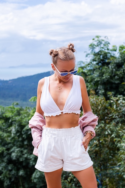 Turista de blogger de mujer con estilo europeo se encuentra en la cima de la montaña con una increíble vista tropical de la isla de Koh Samui Tailandia Moda retrato al aire libre de mujer