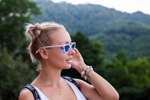 Turista de blogger de mujer con estilo europeo se encuentra en la cima de la montaña con una increíble vista tropical de la isla de Koh Samui Tailandia Moda retrato al aire libre de mujer