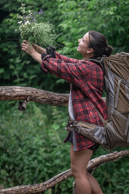 Turista chica atractiva con una mochila grande para viajar y con un ramo de flores silvestres.