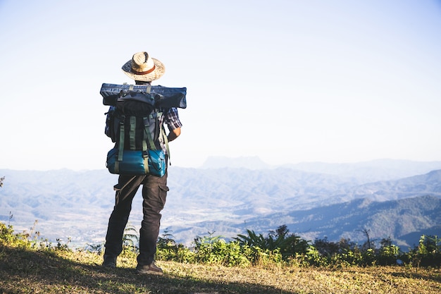 Turista desde la cima de la montaña. rayos de sol. hombre usa mochila grande contra la luz del sol