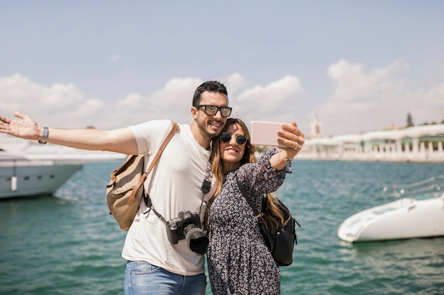 Turista feliz de los pares que toma el autorretrato a través del teléfono celular delante del mar