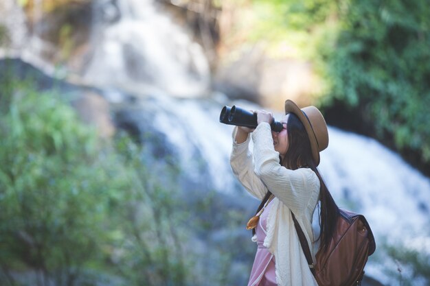 Turista femenina que está mirando los prismáticos para ver la atmósfera en la cascada