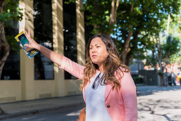 Turista femenina que sostiene el teléfono móvil y el mapa en la mano que intenta llamar un taxi