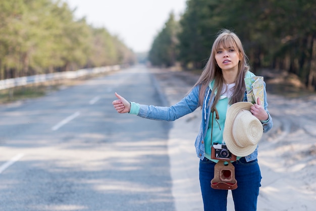 Turista femenino bastante joven que hace autostop a lo largo de un camino