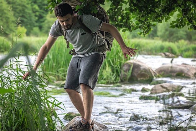 Un turista con una gran mochila de senderismo se está refrescando cerca de un río de montaña en el calor del verano.