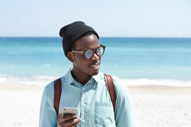 Turista joven de moda en tonos y sombrero con paseo matutino a lo largo de la costa del mar
