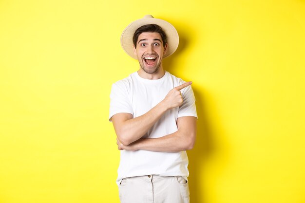 Turista masculino feliz con sombrero de paja apuntando con el dedo hacia la derecha, mostrando la oferta promocional en el espacio de la copia, fondo amarillo. Copia espacio