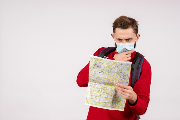 Turista masculino de vista frontal en máscara estéril explorando el mapa en la pared blanca