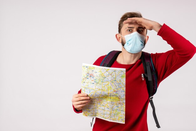 Turista masculino de la vista frontal en la máscara estéril que sostiene el mapa en la pared blanca