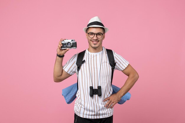 Turista masculino de la vista frontal que toma la fotografía con la cámara en el color de las emociones del turista de la pared rosada