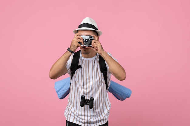 Turista masculino de la vista frontal que toma la fotografía con la cámara en el color de las emociones del turista de la pared rosada