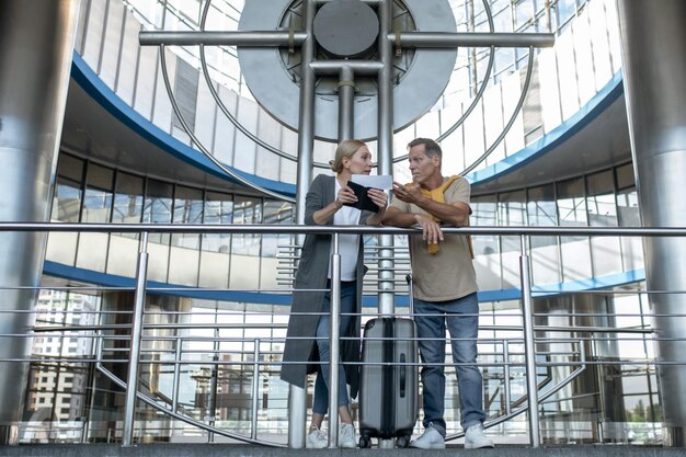 Turista de mediana edad enfocada con boletos hablando con su compañero masculino en la terminal del aeropuerto