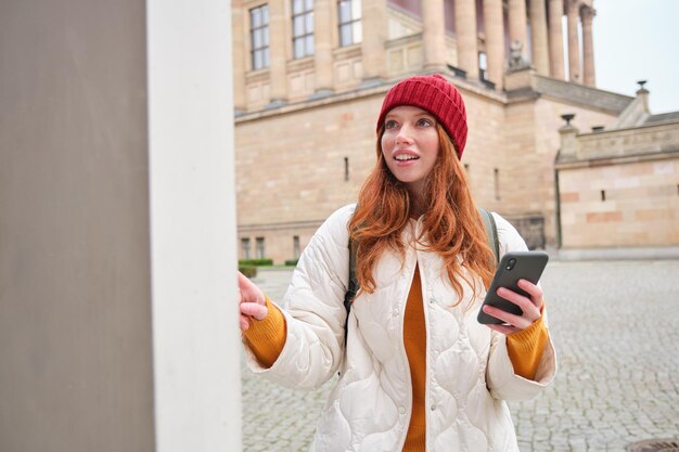 Una turista pelirroja sonriente camina por la ciudad y explora lugares de interés populares con sm
