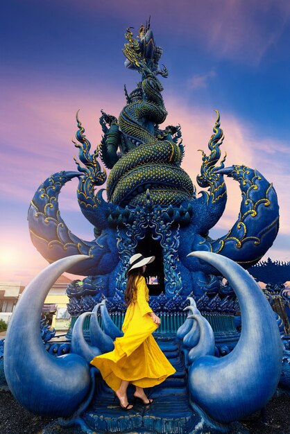 Turista usa vestido amarillo y de pie en la estatua azul en Chiang Rai, Tailandia