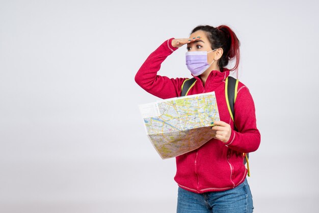 Turista de vista frontal con mapa en máscara en la pared blanca