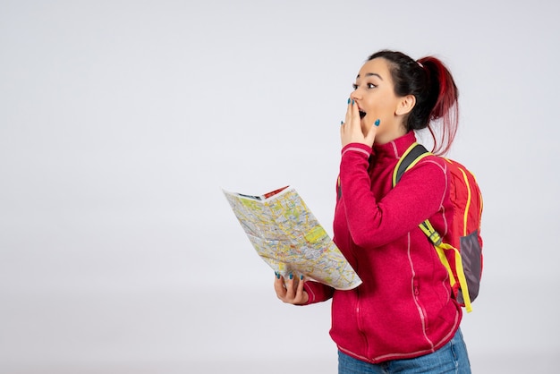 Turista de vista frontal con mochila y mapa en la pared blanca