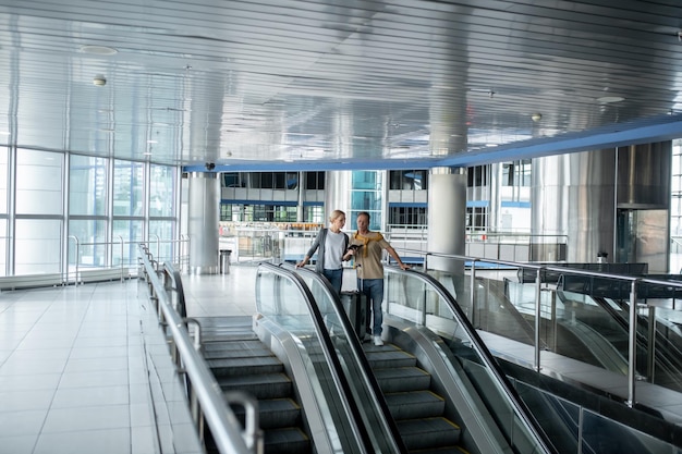 Turistas concentrados examinando un documento de viaje en la escalera mecánica del aeropuerto