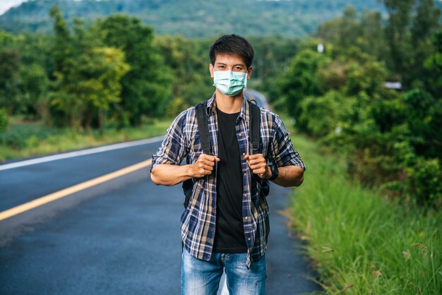 Turistas hombres con una máscara, llevando una mochila en el camino.