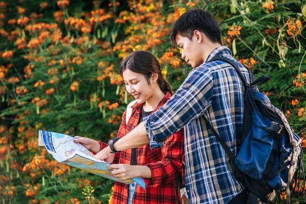 Los turistas hombres y mujeres miran el mapa cerca de los jardines de flores.