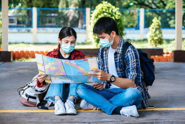 Los turistas masculinos y femeninos miran el mapa al lado del ferrocarril.