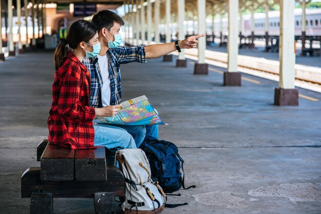 Los turistas masculinos y femeninos miran el mapa al lado del ferrocarril.