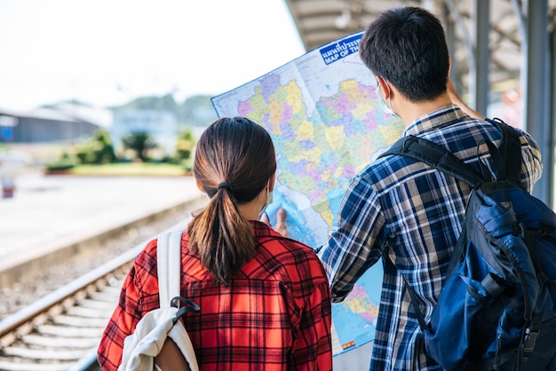 Los turistas masculinos y femeninos miran el mapa al lado de las vías del tren.