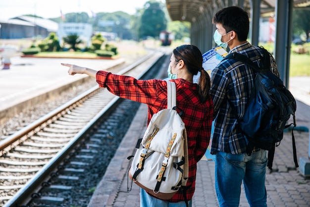 Los turistas masculinos y femeninos miran el mapa al lado de las vías del tren.