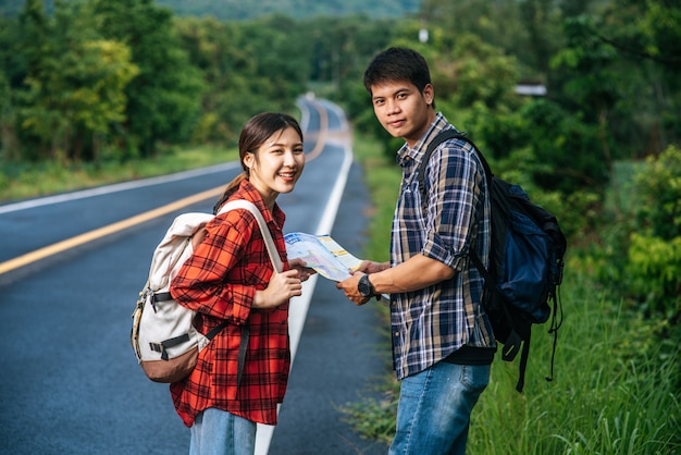 Los turistas masculinos y femeninos miran el mapa en el camino.