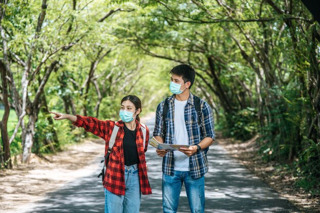 Los turistas masculinos y femeninos usan máscaras médicas y miran el mapa en la calle.