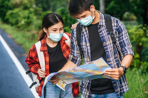 Los turistas masculinos y femeninos usan máscaras médicas y miran el mapa en la calle.