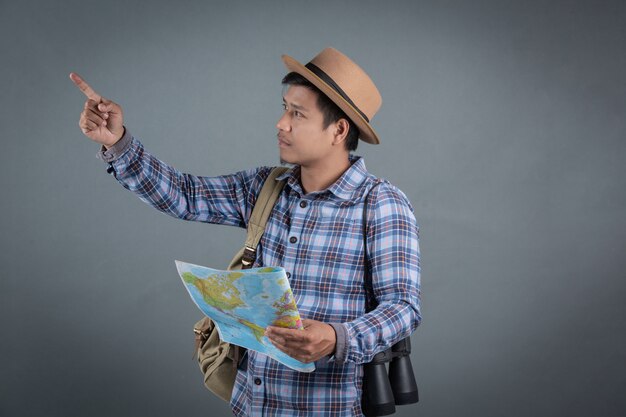 Turistas masculinos que llevan las mochilas que llevan un mapa gris del fondo.