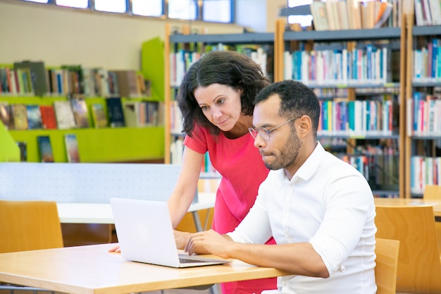 Tutor ayudando a estudiantes con investigación en biblioteca