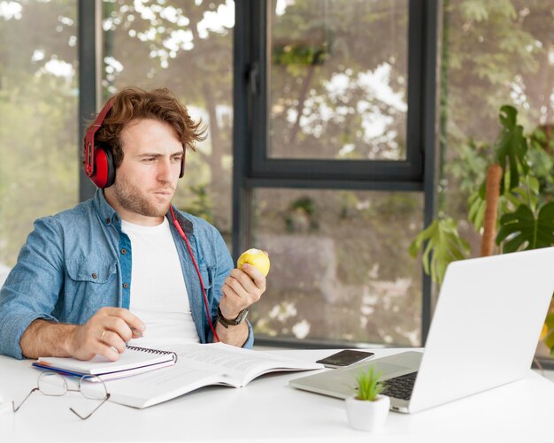 Tutor en casa comiendo una manzana y sentado en su escritorio